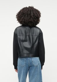 Mustmust nahkjackett sileda viimistlusega, pehmete mustade varrukatega, karedaks helesinine teksapüksid.