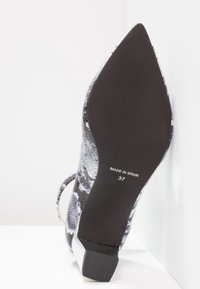 Chaussure à talons hauts avec un motif en cuir de serpent gris et noir. Talon carré avec une semelle texturée. Marquée "FABRIQUÉ EN ESPAGNE" et taille 37.
