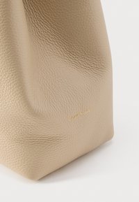 Borsa a mano in pelle beige con superficie strutturata e base rettangolare, caratterizzata da un marchio discreto color oro. Aspetto liscio e morbido.