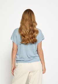 Maglioncino a maniche corte color azzurro chiaro con vestibilità ampia e leggero luccichio. Presenta una scollatura rotonda e orlo a coste, abbinato a pantaloni color crema.