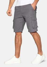 Graue Cargo-Shorts aus leichtem Material, ausgestattet mit mehreren Taschen, gesteppten Details und einem geraden Schnitt. Getragen mit weißen Sneakers.