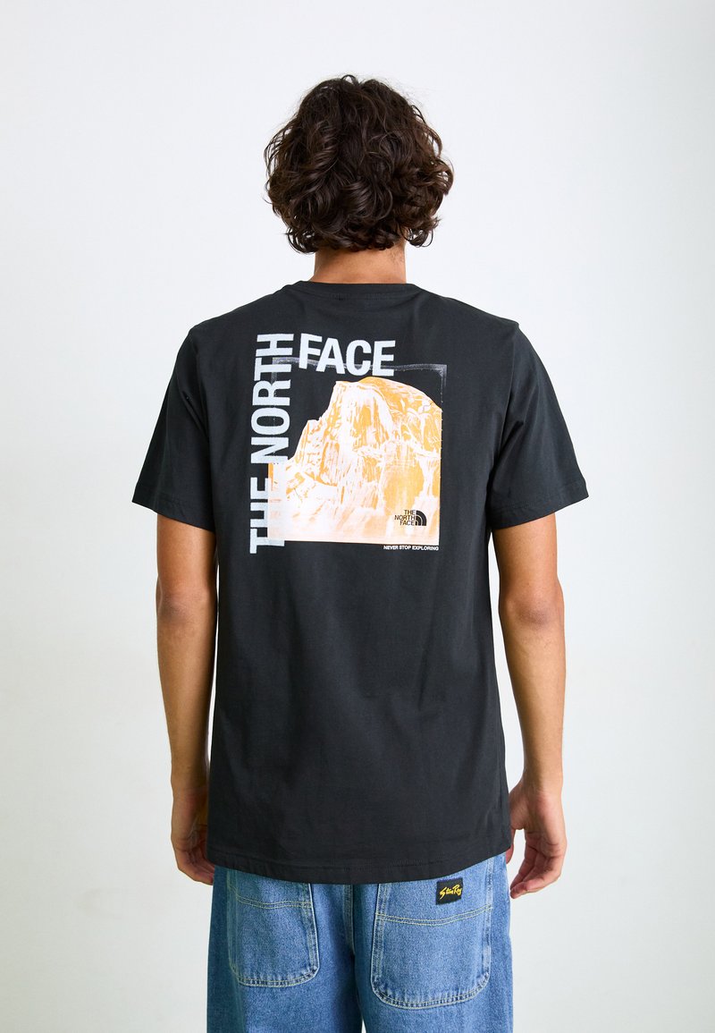 Sort bomulds T-shirt med et stort grafik af et bjerg på ryggen. Accentueret med hvid og orange tekst. Løs pasform, rund halsudskæring.