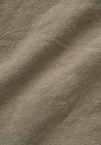 Material bej din in, cu textura țesăturii vizibile și cute naturale care creează umbre fine pe suprafață.