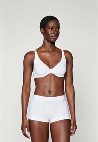 Soutien-gorge blanc avec un design lisse et sans couture et des bretelles ajustables, associé à un shorty blanc avec une taille douce et des coutures minimales.