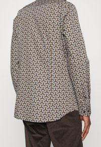 Patroond shirt in bruin, wit en geel met een ingewikkeld, golvend ontwerp. Lange mouwen, knoopmanchetten en een gebogen zoom. Gemaakt van katoen.