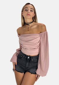 Skulderfri, lyserød top med samlet front og lange, gennemsigtige ærmer, parret med sorte slidte denim shorts. Sort choker som accent.