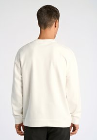 Felpa crema con colletto a giro e maniche lunghe, caratterizzata da un design semplice e polsini a costine, vestibilità rilassata e morbido tessuto di cotone.