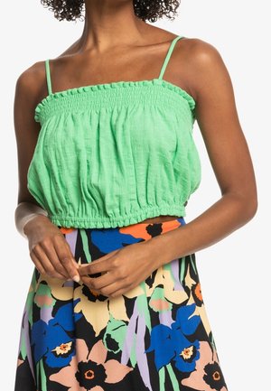 Top corto verde fruncido con tirantes finos; presenta una tela ligera y una cintura fruncida, combinado con una falda estampada de flores en varios colores.