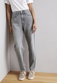  Hoge taille grijze denimbroek met een rechte pijp, voorzien van voorzakken en een knoopsluiting, gecombineerd met lichtgrijze sneakers.