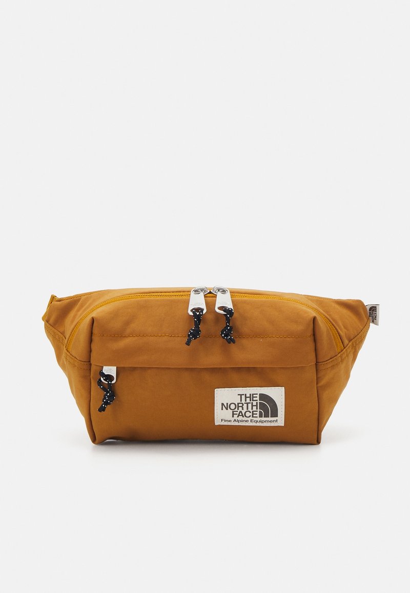 Banane marron avec poche avant zippée et compartiment principal, avec patch logo The North Face et tirettes de fermeture éclair noires avec nœuds.