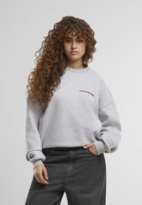 Grå hettegenser med avslappet passform, ribbestrikkede mansjetter og en synlig "PROHIBITED" logo i burgunder. Kombinert med høytlivet svarte jeans.