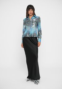 Camisa de manga longa em azul com padrão abstrato, combinada com uma saia preta elegante. O tecido texturizado e a silhueta ajustada realçam o visual.