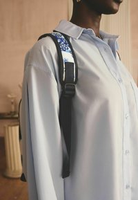 Camisa de botones de color azul claro con un corte relajado, combinada con una correa de patrón que presenta diseños florales azules y una hebilla ajustable negra.