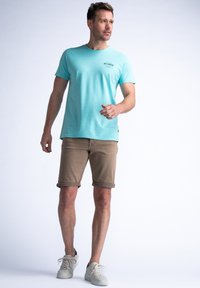 Camiseta de algodón turquesa con cuello redondo, combinada con pantalones cortos beiges y zapatillas blancas. Diseño sencillo sin patrones visibles ni herrajes.