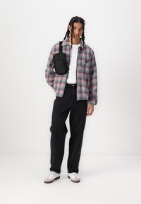 Plaid flannel shirt in pastel colors, white t-shirt, black jeans, and white sneakers with gray accents; small black crossbody bag.