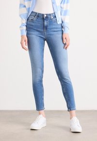 Jeans skinny bleu clair à taille haute, en denim. Présente une finition délavée, cinq poches et des coutures soignées le long des coutures.