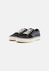 Black suede sneakers with a textured gray panel, green side stripe, beige laces, and a white rubber sole.