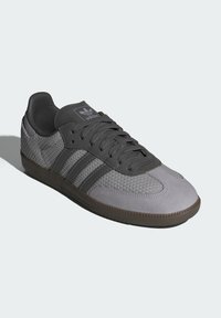 Grå sportskor med mesh-övre, mockadetaljer, gummisula och tre mörkgrå ränder. Har rund snörning och stoppad vristkrage.