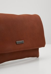 Borsa in pelle marrone con texture, caratterizzata da un design piegato e una placca logo in argento, con una finitura liscia e forma compatta.