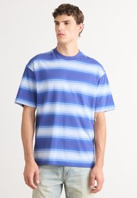 Camiseta de algodón a rayas azules. Presenta rayas horizontales en diferentes tonos de azul, con un corte relajado y mangas cortas.