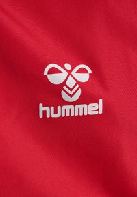 Roter Stoff mit einem weißen Logo, das ein symmetrisches Design zeigt, das einer Biene ähnelt, und dem Wort "hummel" in fetten Buchstaben.