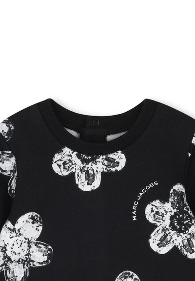 Czarny sweter z wyraźnym białym kwiatowym wzorem, okrągłym dekoltem i prążkowanymi mankietami. Ma mały czarny zamek z tyłu. Widać logo Marc Jacobs.