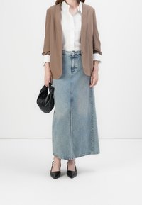 Brun kavaj över en vit skjorta med knappar, paired med en ljusblå denim maxi kjol. En svart handväska och svarta klackar med spetsig tå fulländar looken.