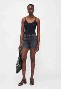 Top negro sin mangas con tirantes finos, shorts de mezclilla oscuros de tiro alto, sandalias planas negras, sosteniendo un bolso negro con patrones circulares blancos.