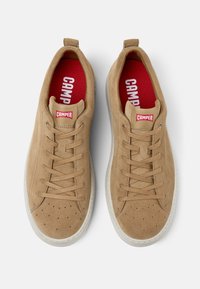 Sneaker in suede beige con punta perforata, design con lacci, suola in gomma bianca e branding rosso "CAMPER" sulla linguetta e nella soletta.