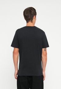 T-shirt de algodão preto com mangas curtas e decote redondo. Textura suave, ajuste standard, sem logótipos ou padrões visíveis nas costas.