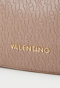 Bežs reljefs ādas soma ar atkārtotu "Valentino" rakstu, ar gludu tekstūru un zelta logotipa plāksni priekšpusē.