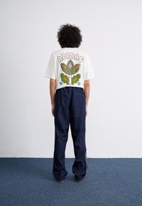 White short-sleeve t-shirt featuring a multicolored graphic on the back and blue denim pants with a relaxed fit and side stripes.