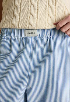 Person wearing cream cable-knit sweater and blue-and-white vertical striped pants with "Joules" brand label at the waistband.