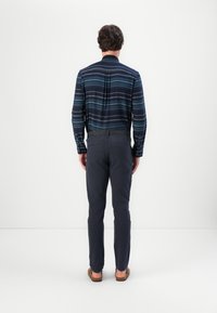 Navy striped button-up shirt with long sleeves, paired with dark gray slim-fit pants and brown slip-on shoes; seen from behind.