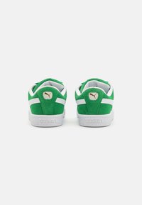 Gröna mockasneakers med vita accenter, med en texturerad gummisula och en guldlogotypdetalj bak. Retrodesign och låg profil.