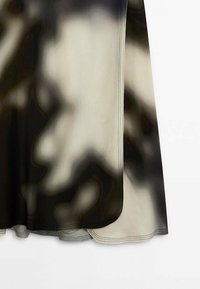 Tissu tie-dye noir, blanc et gris avec coutures surpiquées et ourlet courbé, présentant un bord de vêtement fluide sur un fond blanc.