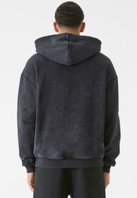 Tamsiai pilka per didelis gobtuvu apnuogintas džemperis, turintis tekstūruotą paviršių, plačią gobtuvo dalį ir dry�žuotas rankoves. Siūlo laisvą siluetą ir minimalistinį dizainą.