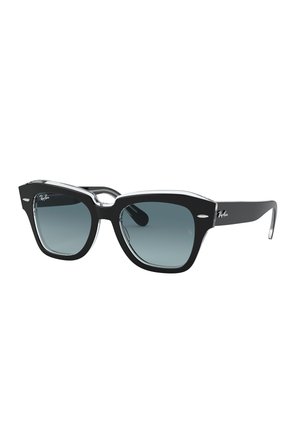 Occhiali da sole neri in plastica con lenti quadrate oversize, dotati di una montatura trasparente, lenti sfumate e un sottile logo Ray-Ban sulla tempia.