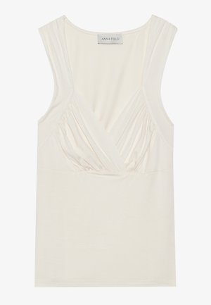 Krēmus krāsas bez piedurknēm topiņš ar V veida kakla izgriezumu un savirknējumu detaļām sānos, izgatavots no mīkstas, elastīgas materiāla. Etiķete norāda "ANNA FIELD."