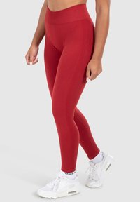Leggings rossi a vita alta con una texture liscia, con dettagli laterali discreti, abbinati a sneakers sportive bianche.