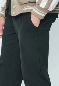 Pantalons noirs à coupe décontractée, avec poches latérales. La taille est élastiquée pour plus de confort, et le tissu semble lisse et léger.