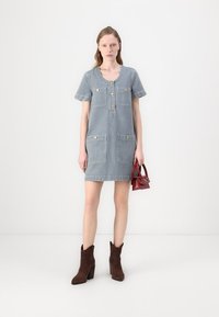 Rochie din denim în dungi, cu mâneci scurte, închidere cu nasturi și două buzunare frontale. Purtați cu botine maro și o geantă mică roșie.
