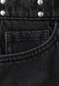 Tissu en denim noir avec une poche et des détails de couture, avec une rangée de clous ronds argentés également espacés au-dessus de la poche.