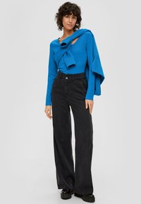 Blaues langärmliges Oberteil mit rundem Halsausschnitt und gerafftem Akzent, kombiniert mit hochtaillierten schwarzen weiten Hosen und klobigen Schuhen.