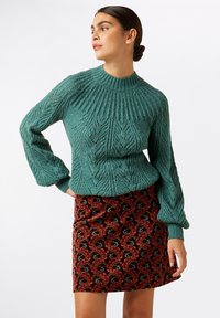 Tyrkis strikket sweater med en ribbet halsudskæring og indviklede bladmønstre, parret med en bordeaux nederdel med et farverigt bølgemønster.