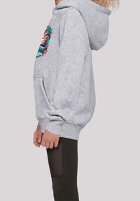 Sudadera gris con un diseño gráfico colorido en el frente, que presenta un bolsillo canguro y puños de canalé. Combinada con leggings negros con detalles de malla.