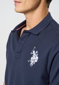 Námornícky polo tričko vyrobené z bavlny s štruktúrovaným povrchom. Obsahuje bielo vyšívané logo na ľavej hrudi a kontrastný golier.