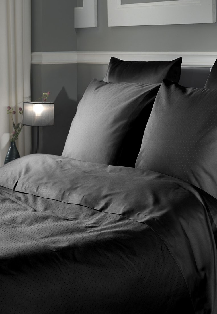 Schwarzes Bettwäsche-Set mit glatter Textur, gepunktetem Muster und zwei passenden Kissenbezügen, ordentlich auf einem Bett arrangiert.