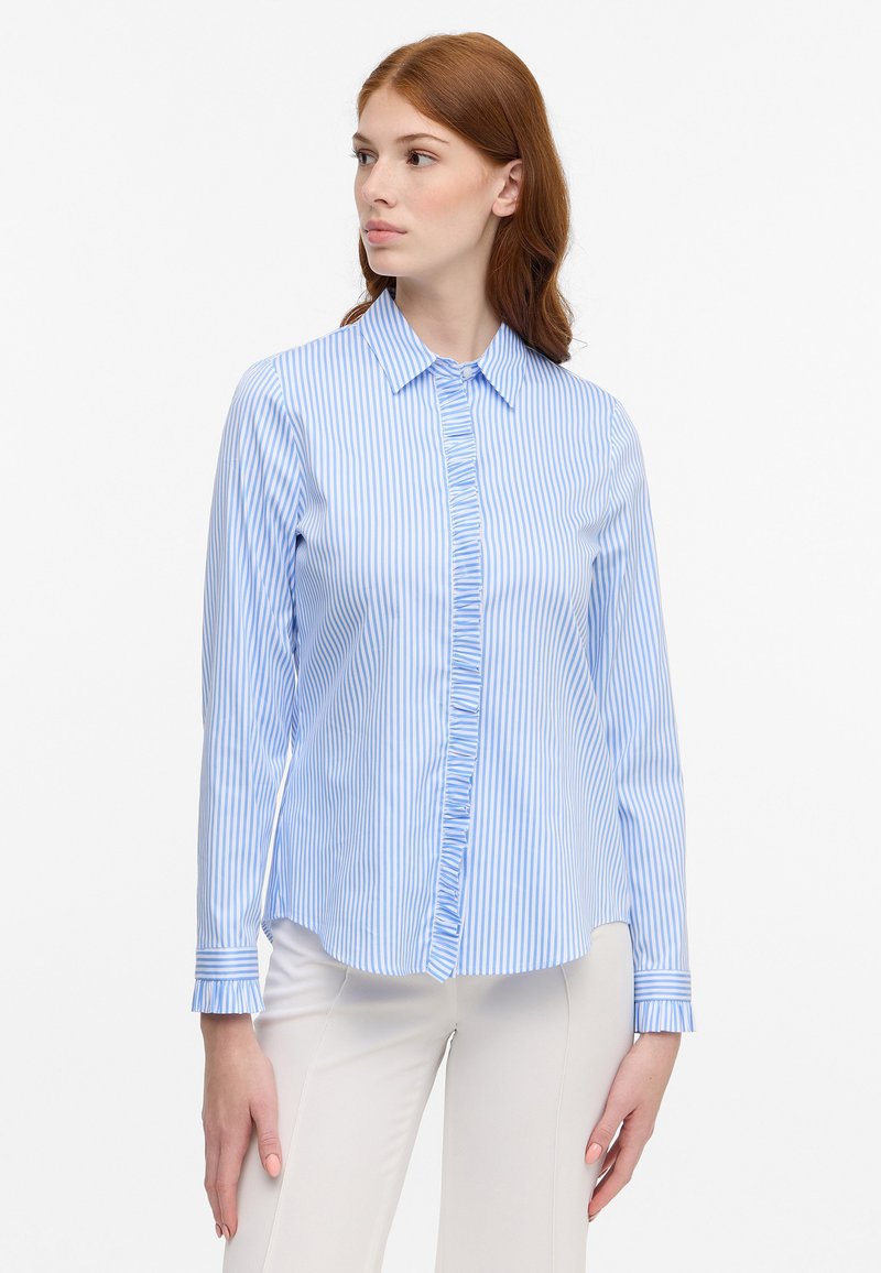 Blue and white striped button-up shirt with ruffled front, long sleeves, and folded cuffs. Made of a smooth fabric with a tailored fit.