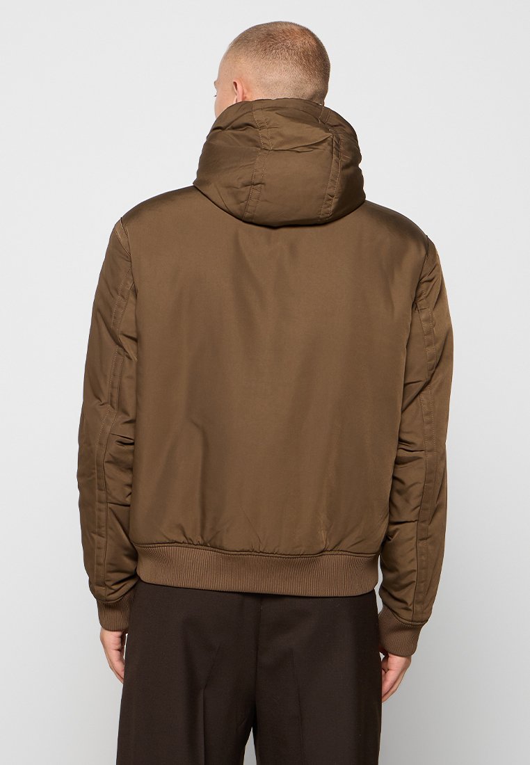 Veste bomber isolée marron avec capuche, poignets et ourlet élastiques, présentant une texture lisse et un design minimaliste.